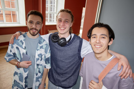 Portrait of multiethnic group of three happy male fellow students smiling looking at camera while posing together in university hallway, camera flashの写真素材