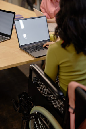 Vertical cropped shot of unrecognizable female wheelchair user working on laptop with blank mockup...