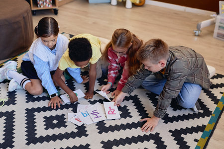 High angle view at group of young children laying alphabet cards on floor while learning English in school togetherの写真素材