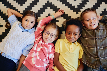 Top down view of multiethnic group of children laying on floor together in classroom and looking up at camera smilingの写真素材