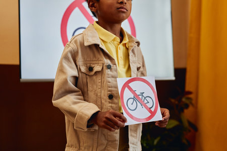 Close up of young African American boy holding No bicycles sign while giving presentation on road safety in primary school classroom copy spaceの写真素材