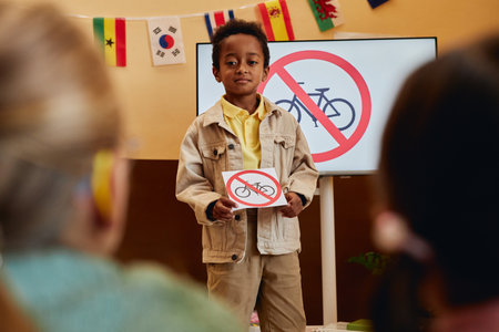 Waist up portrait of young boy holding No bicycles sign while giving road safety presentation to children in school classroom copy spaceの写真素材