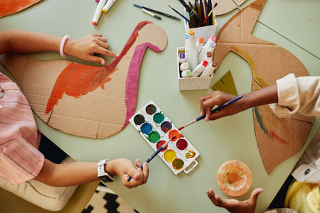 Top down view at group of children painting cardboard dinosaur figures using colorful watercolors during art and craft class copy spaceの写真素材