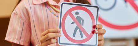 Header image of young girl holding No bicycles sign while learning road safety rules for children in primary school classroom copy spaceの写真素材