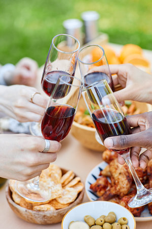Close-up of hands raising wine glasses during picnic including snacks, olives, and crackers on table. Cheers and camaraderie in outdoor setting with diverse participantsの写真素材