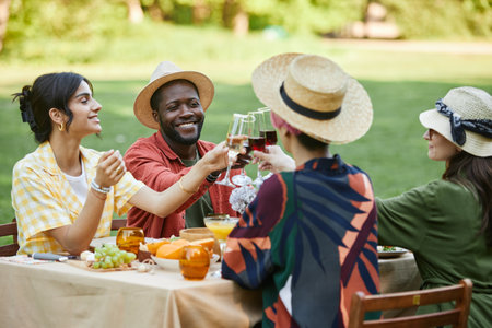 Group of friends enjoying picnic outdoors, sharing food and drinks in sunny park setting....