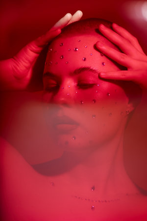 Distorted closeup portrait of bald young woman with crystal makeup looking away posing confidently...