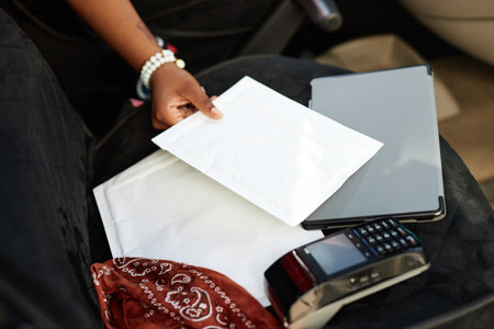 Person in car handling delivery papers alongside electronic devices including a tablet and a receipt...