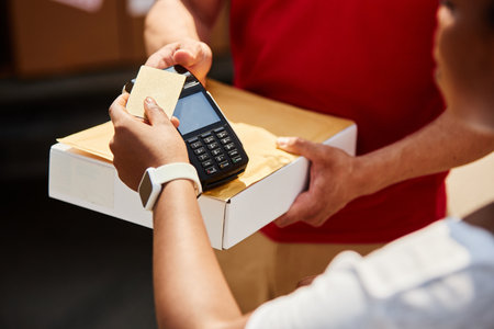 Close-up of persons hands conducting credit card payment transaction using card reader with box on counter, wearing white smartwatch on wrist, illustrating modern retail exchangeの写真素材
