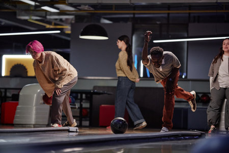 Group of friends engaging in competitive game of bowling in a modern, illuminated bowling alley...