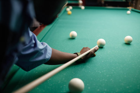 Close-up of person in blue shirt playing billiards on green pool table showing cue stick and balls. Concentration and strategy involved in shotの写真素材