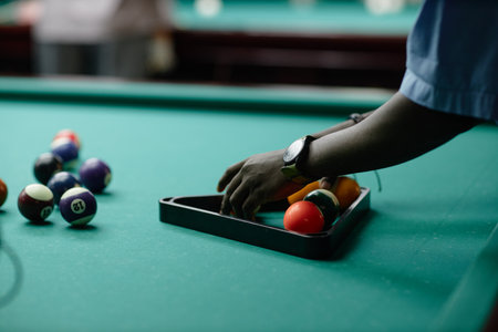 Hand arranging colorful billiard balls on table with focused precision, watch visible on wrist capturing moment of preparation before game beginsの写真素材