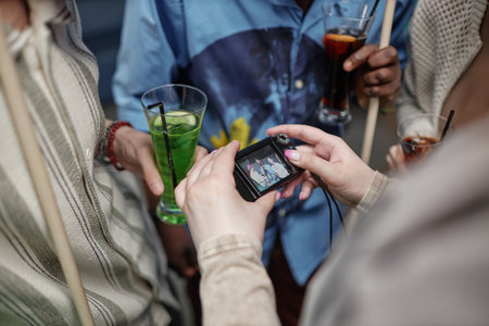 Group of people socializing, holding drinks while someone is taking a picture with a compact digital camera during gatheringの写真素材