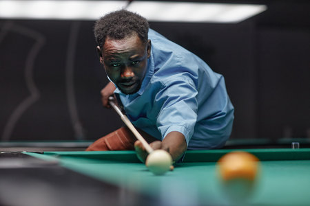 Man focusing on game of billiards, aiming cue ball with intense concentration, ensuring precise shot and formの写真素材