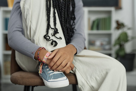 Close up detail shot of Black teenage girl wearing canvas shoes and colorful handmade friendship bracelets sitting on chair with leg up copy spaceの写真素材
