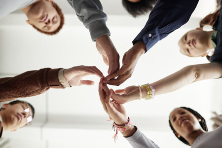 From below shot of group of children touching hands during team building exercise in school or at...