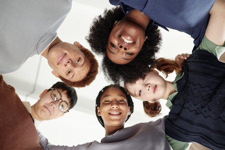 From below shot of diverse group of teenage kids with teacher standing in circle looking down at...