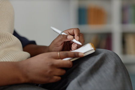 Side view closeup of unrecognizable Black young woman writing in notebook and taking notes during lecture or seminar, focus on hands holding pen, copy spaceの写真素材
