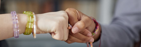 Close up of two unrecognizable teenagers doing fist bump in school hands wearing friendship...
