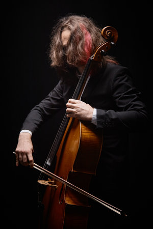 Vertical shot of passionate unrecognizable male musician with pink lock of long hair playing cello...