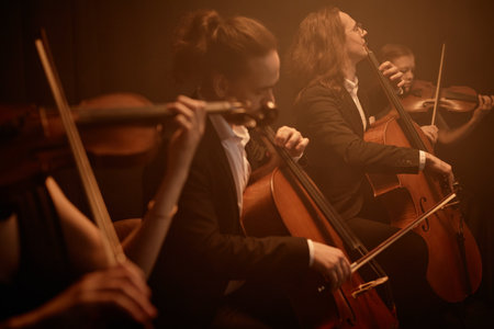 String quartet passionately playing cellos and violins while sitting in row on stage in misty orange light, copy spaceの写真素材