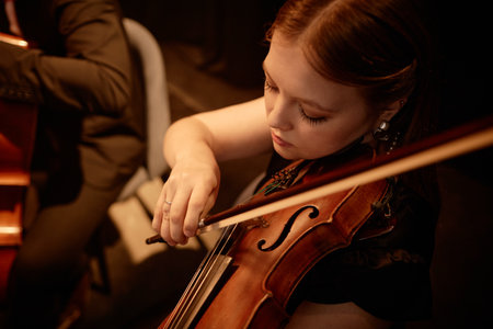 High angle shot of concentrated female violinist performing classical music on stage in warm lightの写真素材