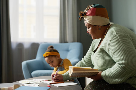 Minimal side view portrait of mature African-American woman teaching alphabet to cute little girl in...