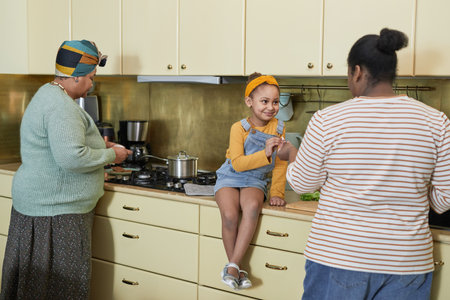 Portrait of happy African-American family cooking dinner together focus on cute smiling girl sitting...