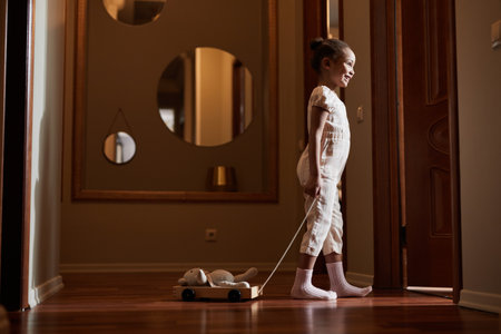 Candid full length portrait of cute African-American girl peeking in parents bedroom while standing in sunlit hall, copy spaceの写真素材