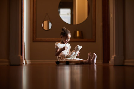 Candid full length portrait of cute African-American girl playing with toys at home while sitting on floor in hall lit by sunlight, copy spaceの写真素材