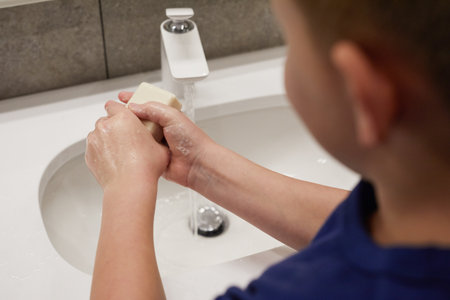 High angle close up of little boy washing hands at sink and holding soap, hygiene and COVID protection concept, copy spaceの写真素材