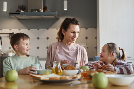 Portrait of mother looking at girl with down syndrome while sitting at dining table and enjoying breakfast together with family, copy spaceの写真素材