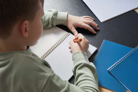 High angle close up of boy writing in notebook while doing homework or studying at desk, copy spaceの写真素材