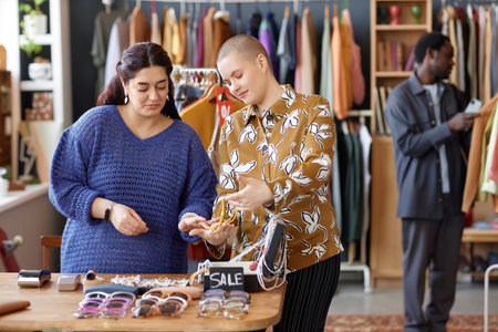 Medium shot of young woman with buzz cut choosing fashion accessories with Middle Eastern female...
