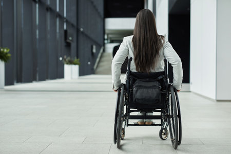 Back view full length at young businesswoman in wheelchair entering office building, copy spaceの写真素材