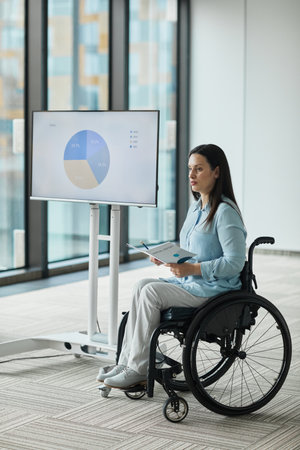 Vertical full length portrait of successful businesswoman in wheelchair leading team meeting and...