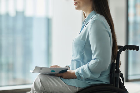 Cropped side view portrait of young businesswoman in wheelchair holding booklet while giving speech or attending conference, copy spaceの写真素材