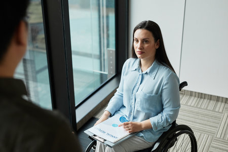 High angle view at young businesswoman in wheelchair talking to male colleague in office, copy spaceの写真素材