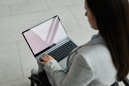 High angle portrait of young businesswoman in wheelchair using laptop with blank white screen, copy spaceの写真素材