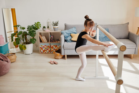 High angle view at cute ballerina with down syndrome standing by bar at home and doing stretching exercise, copy spaceの写真素材