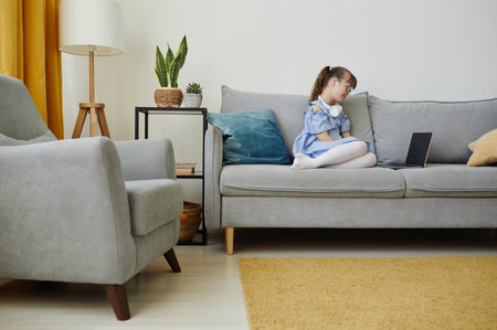 Side view portrait of teenage girl with downs syndrom using laptop at home while sitting on couch, copy spaceの写真素材