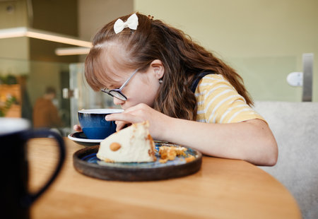 Candid side view portrait of cute girl with down syndrome enjoying desserts in cafe, copy spaceの写真素材