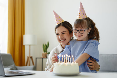 Portrait of happy mother and daughter celebrating birthday and blowing candles by laptop