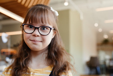 Portrait of cute teenage girl with down syndrome looking at camera in cafe, copy spaceの写真素材
