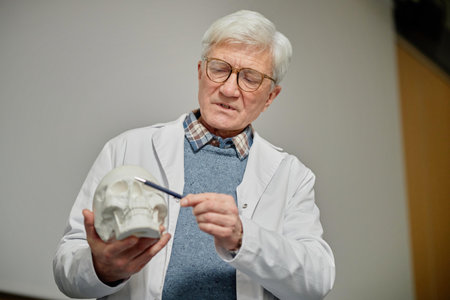 Waist up of portrait of senior professor teaching medicine in class and pointing at human skull...