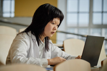 Side view portrait of young Asian woman as med student using laptop during lecture in college or university, copy spaceの写真素材
