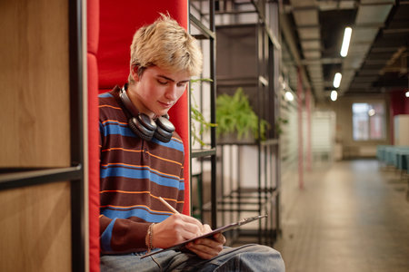 Side view of teenage boy writing notes while sitting in lounge booth