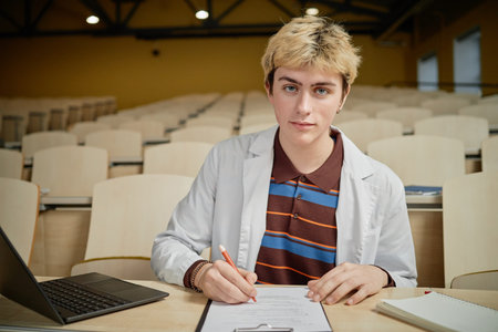 Side view of young male med student writing notes on clipboard during lecture in university, copy spaceの写真素材