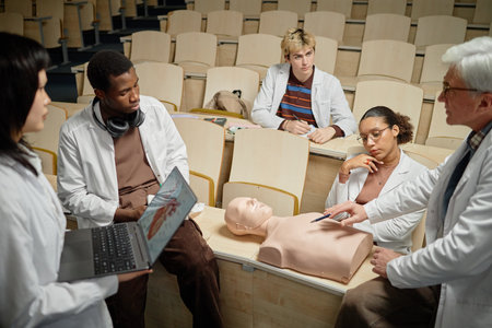 Diverse group of med students watching CPR procedure training on dummy while senior professor pointing at chest during practical lecture in collegeの写真素材