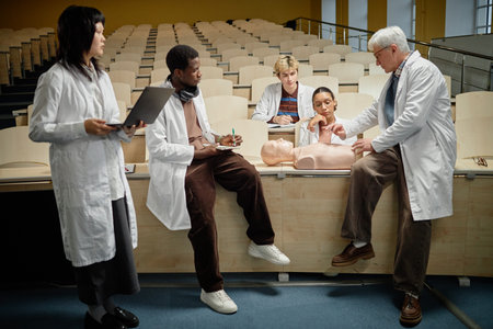 Side view group shot of professor pointing at torso dummy while teaching CPR to diverse med students during class in collegeの写真素材